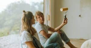 A young couple sits indoors planning their home renovation with a paint roller. Spring Sales