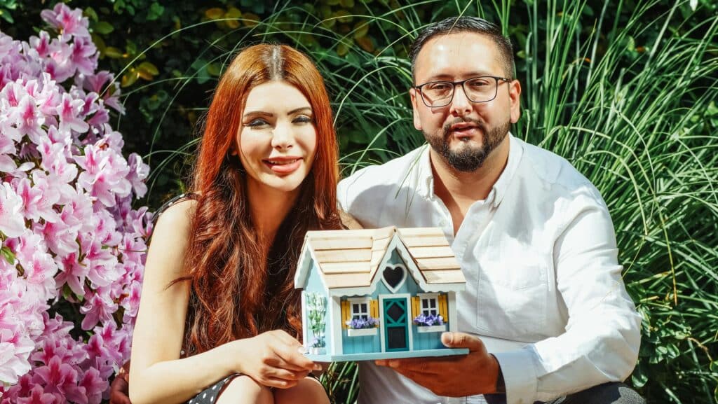 A smiling couple holding a model house, symbolizing homeownership dreams.