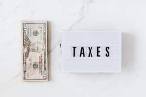 Overhead view of a fifty-dollar bill and a lightbox with 'TAXES' on a marble surface.